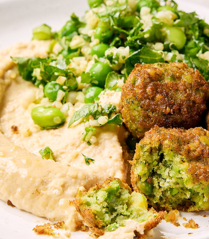 A plate features creamy hummus, crispy falafel, and a fresh herb salad with green beans and bulgur, beautifully arranged.