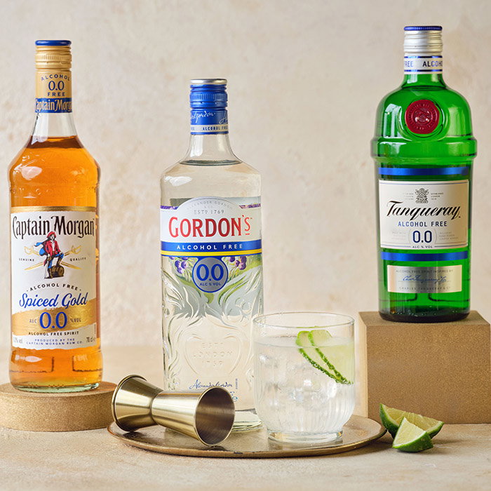 Three bottles of alcohol-free spirits: Captain Morgan, Gordon’s, and Tanqueray, displayed with a glass of mixed drink and a jigger.