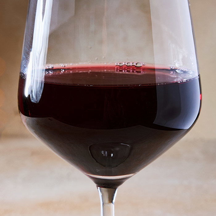 A close-up of a wine glass filled with swirling red wine, set against a soft, neutral background.