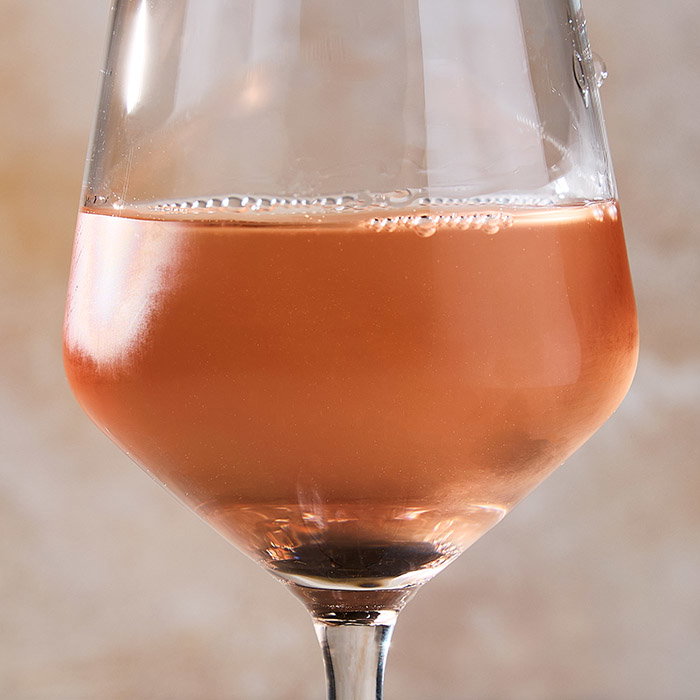 A close-up of a wine glass filled with swirling ros&eacute; wine, set against a soft, neutral background.