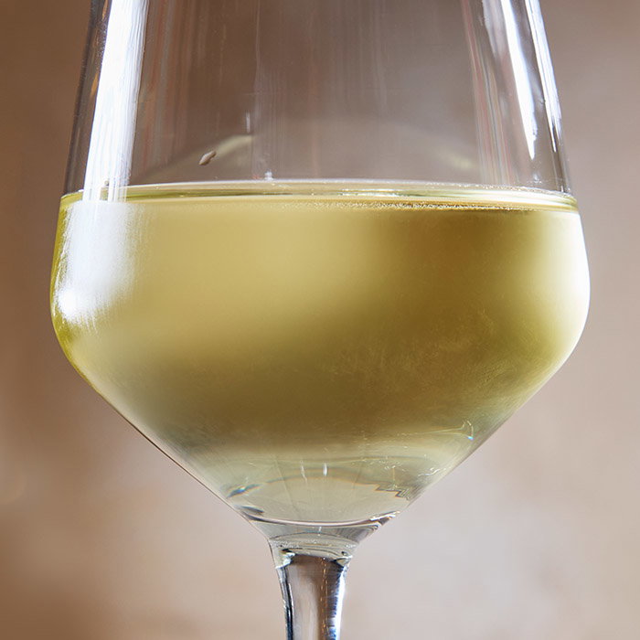 A close-up of a wine glass filled with swirling white wine, set against a soft, neutral background.