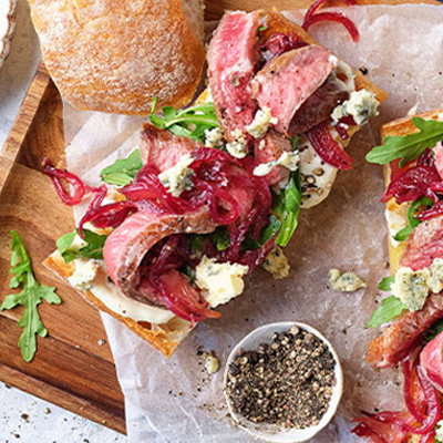 Grilled steak slices topped with red onion, served with roasted potatoes and pickled red cabbage on a wooden platter.