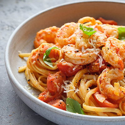 A bowl of prawn pasta topped with fresh basil and Parmesan cheese, featuring vibrant tomatoes and linguine in a savoury sauce.