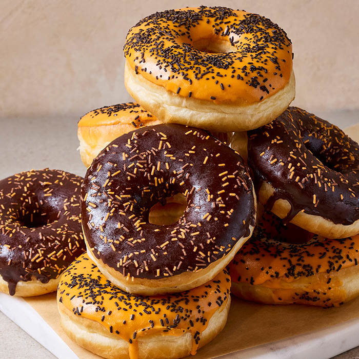 A tempting stack of donuts featuring orange and chocolate glazes topped with black and orange sprinkles, set on a light background.