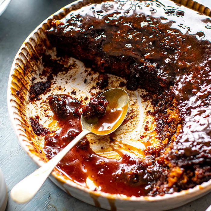 An empty dish with remnants of sticky toffee pudding and a silver spoon, indicating a delicious dessert enjoyed.