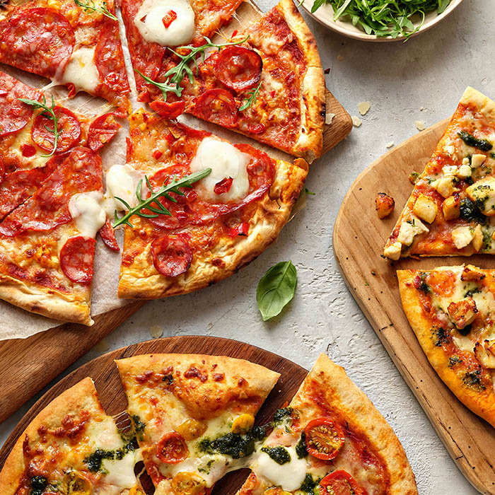 A variety of delicious pizzas, topped with pepperoni, mozzarella, and vegetables, served on wooden boards with fresh greens in a bowl.