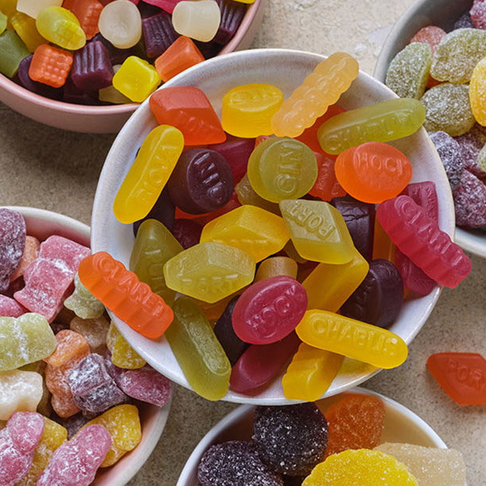 A variety of coluorful gummy candies in bowls, featuring different shapes and flavors, arranged on a neutral surface.