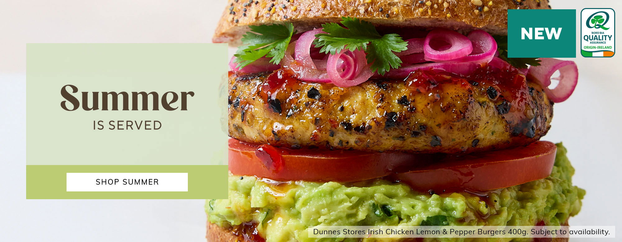 Close-up of a gourmet Irish chicken burger with lemon and pepper seasoning on a seeded bun, topped with fresh tomato slices, red onion rings, cilantro, and smashed avocado. The burger sits on a light green background with text reading 'Summer IS SERVED' and a white 'SHOP SUMMER' button. A teal 'NEW' badge and Irish Quality Assurance logo are visible in the top right corner. Small text at bottom indicates 'Dunnes Stores Irish Chicken Lemon & Pepper Burgers 400g. Subject to availability