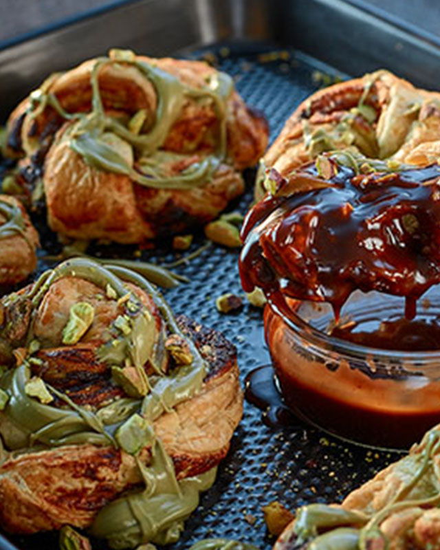 Golden pistachio pastry knots arranged on a baking tray, drizzled with glaze and sprinkled with crushed pistachios