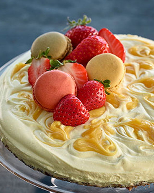 Creamy lemon curd cheesecake topped with strawberries, macarons and lemon zest, served on a cake stand