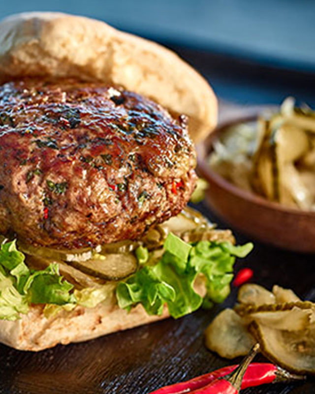 Juicy lamb burger in a toasted bun with pickles on the side