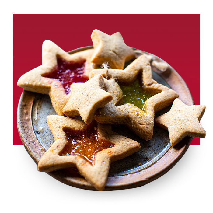 Star-shaped jam biscuits on a ceramic plate with festive red and orange fruit fillings.