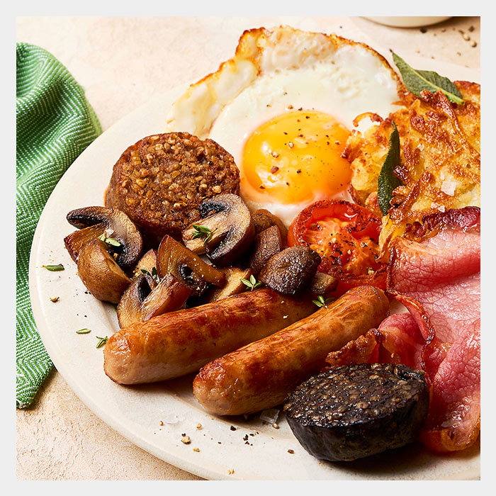 A hearty breakfast plate featuring a fried egg, sausages, mushrooms, tomatoes, bacon, black pudding, and hash brown.
