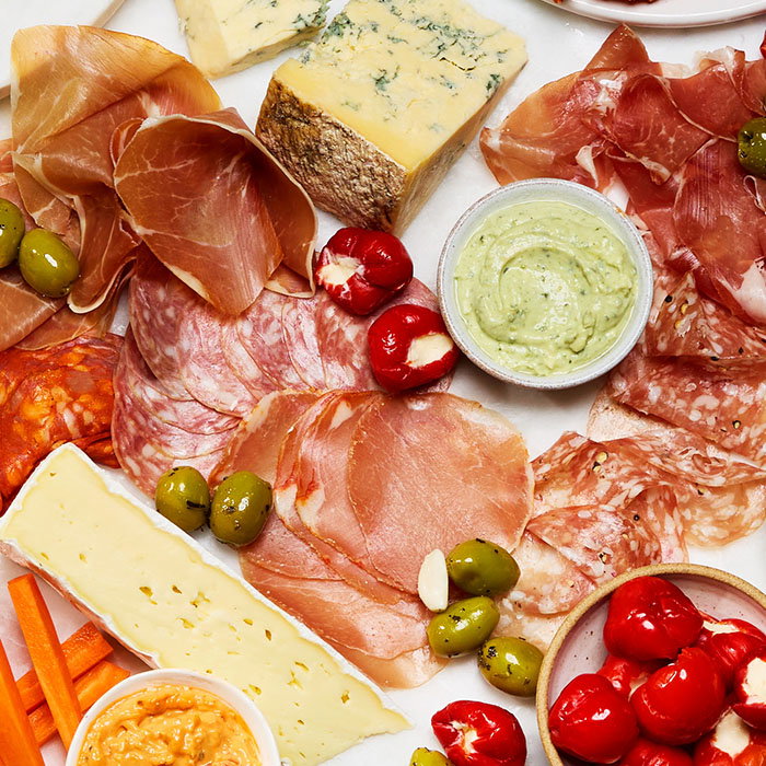 Cheese and charcuterie board with assorted cured meats, cheeses, stuffed red peppers, green olives, and dips.