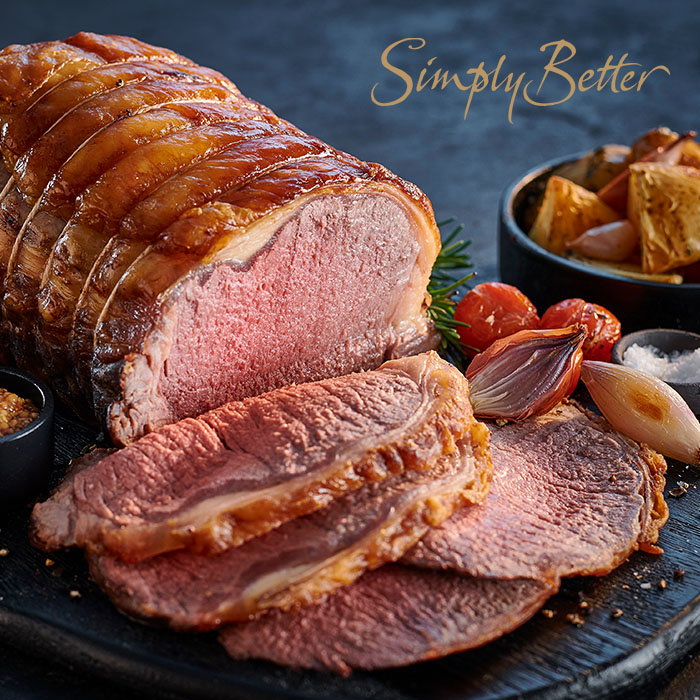 Sliced roast beef with crispy edges served with roasted vegetables, garlic, mustard, and sea salt on a dark board, text 'Simply Better' above.
