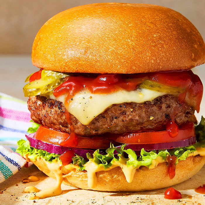 Close-up of a cheeseburger with lettuce, tomato, pickles, onions, melted cheese, ketchup, and sauce in a toasted bun..
