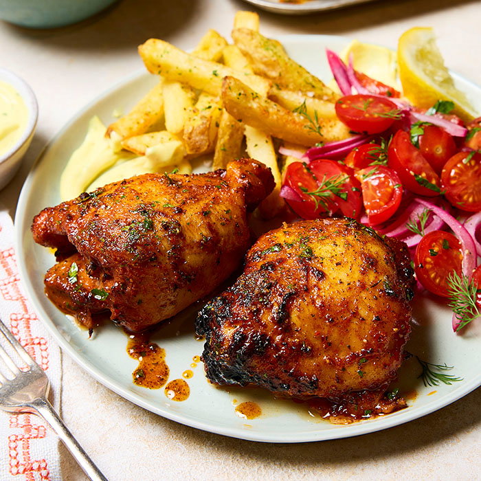 Plate with two pieces of seasoned roasted chicken, French fries, and a salad of cherry tomatoes, red onions, dill, and lemon wedge.