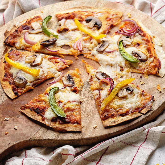 Thin-crust vegetable pizza with mushrooms, bell peppers, and red onions on a wooden cutting board over a striped cloth.