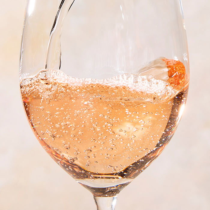 A close-up of sparkling ros&eacute; wine being poured into a clear wine glass with bubbles rising. Links to a wine cellar page showcasing wine products