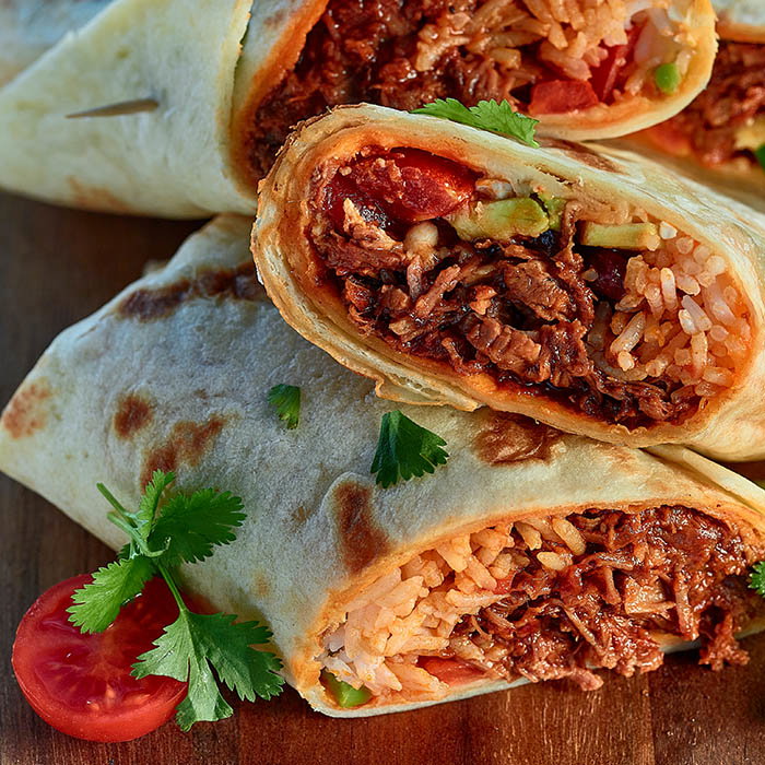 Close-up of beef and rice burritos garnished with cilantro and a sliced cherry tomato on a wooden surface.