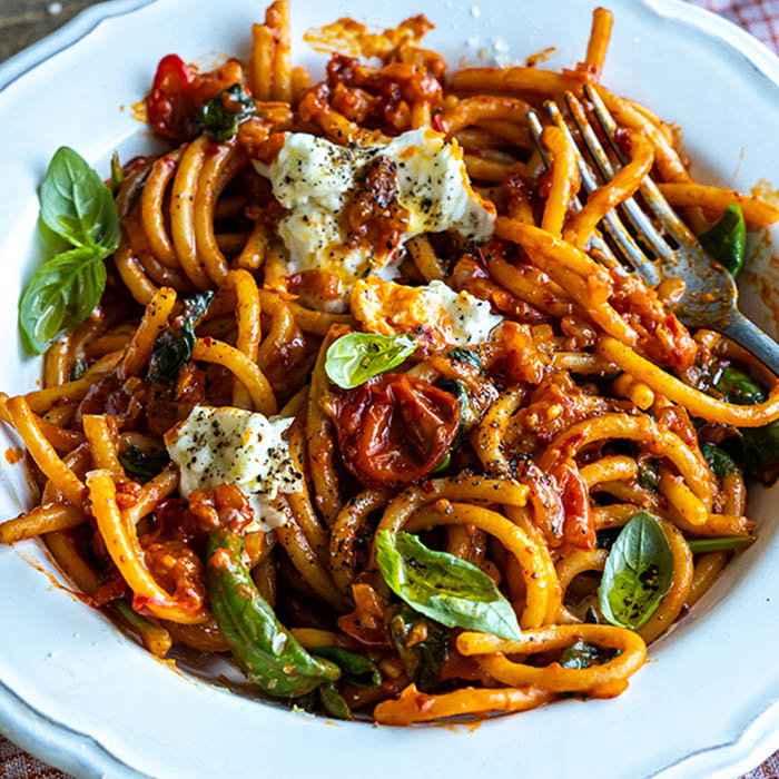 Plate of pasta with tomato sauce, cherry tomatoes, fresh basil leaves, dollops of ricotta cheese, and a fork.