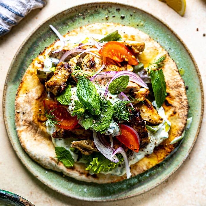Grilled chicken with tomatoes, red onions, fresh herbs, and sauce served on flatbread on a green plate.
