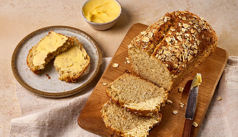 Irish oat soda bread on a wooden board with slices cut, served with butter and oats scattered on top
