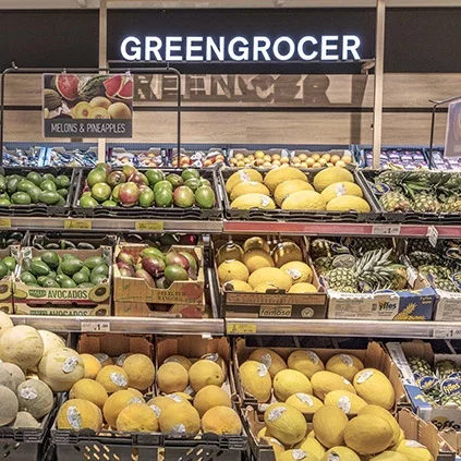 Fresh produce section of a Dunnes Stores store showing wooden crates filled with various fruits including oranges, lemons, and melons under a 'GREENGROCER' sign