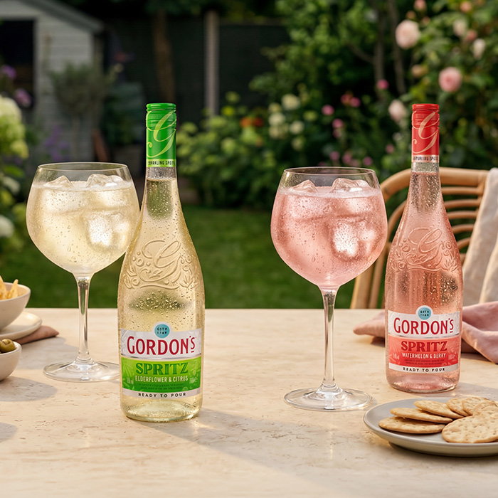 Two bottles of Gordon&rsquo;s Spritz, elderflower and citrus and watermelon and berry, served with ice-filled glasses and light snacks on an outdoor garden table.