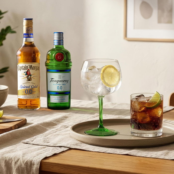 A cozy setting featuring two non-alcoholic beverage bottles, a sparkling drink with lemon, and a glass of cola with lime, on a table.