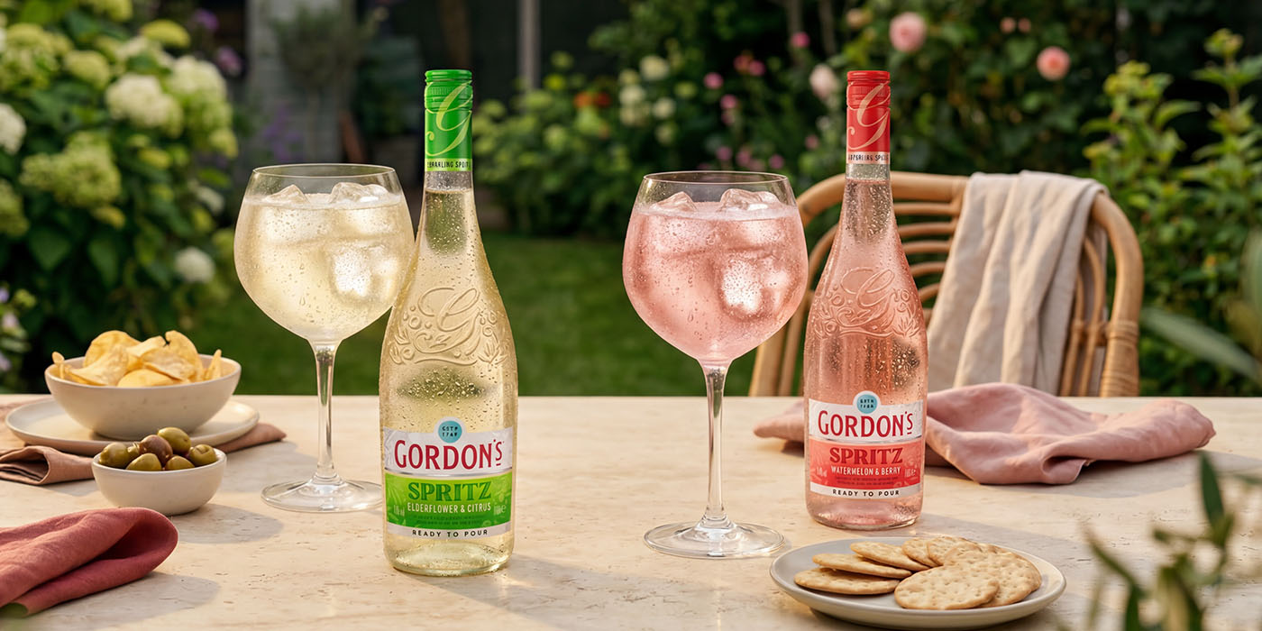 Two bottles of Gordon’s Spritz, elderflower and citrus and watermelon and berry, served with ice-filled glasses and light snacks on an outdoor garden table.