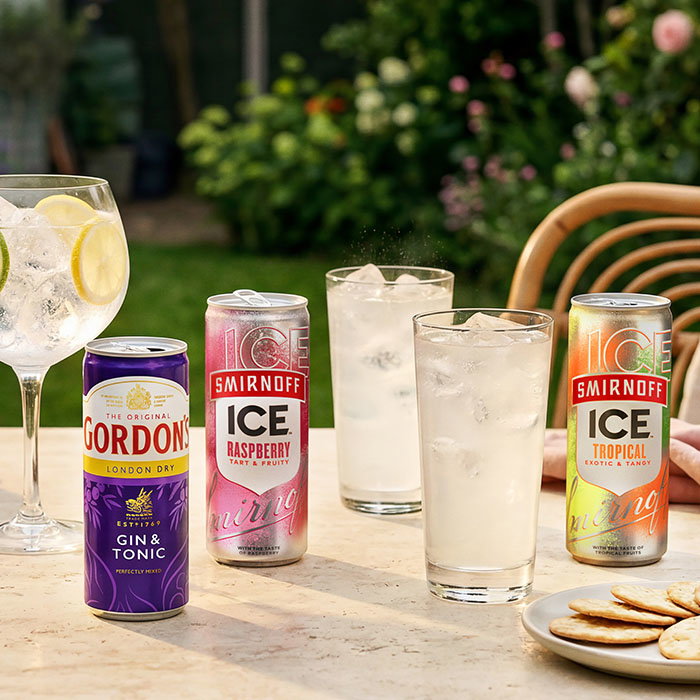 Three cans of Smirnoff Ice and Gordon's Gin & Tonic with glasses of ice and a plate of crackers on a table outdoors.