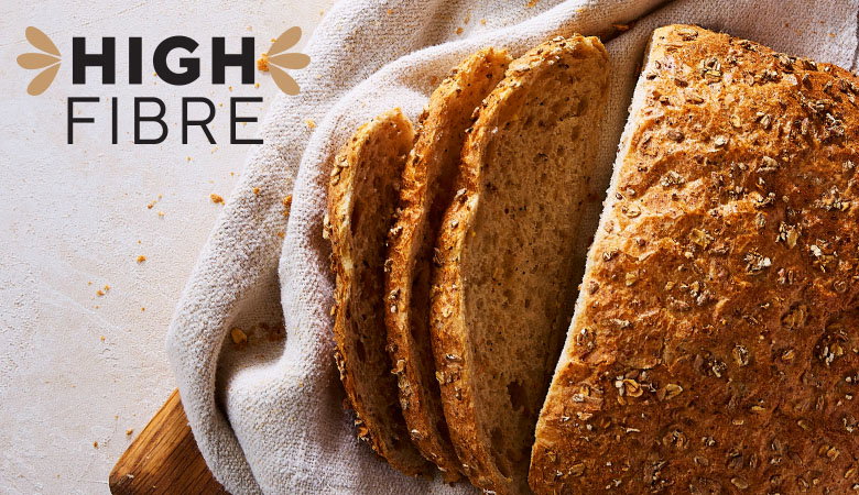 Sliced high-fibre whole grain bread resting on a cloth with "HIGH FIBRE" text beside it.