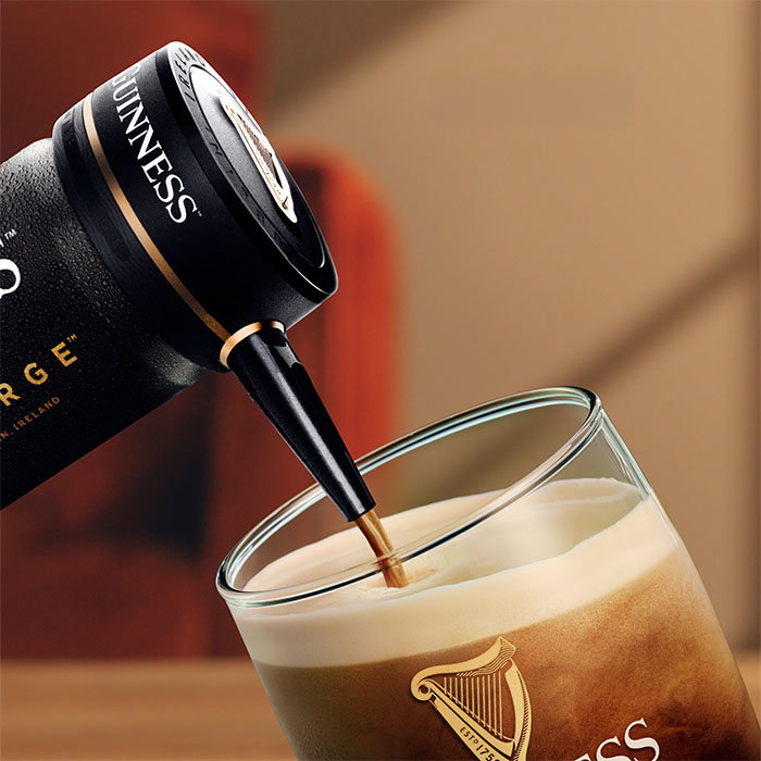 Guinness Nitrosurge device pouring stout into a branded Guinness glass with a creamy head forming