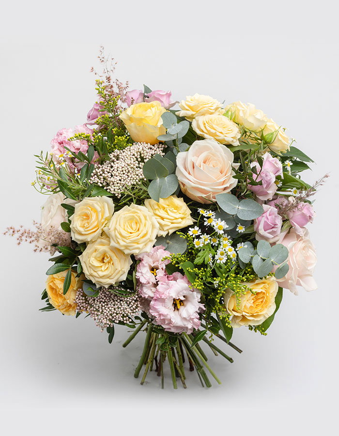 Bouquet of yellow, pale pink, and white roses mixed with eucalyptus leaves and delicate small flowers on a plain background.