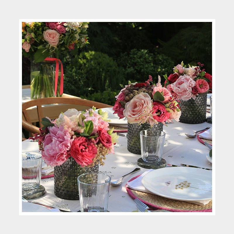 A beautifully set outdoor table featuring decorative floral arrangements in textured vases, with glassware and elegant tableware