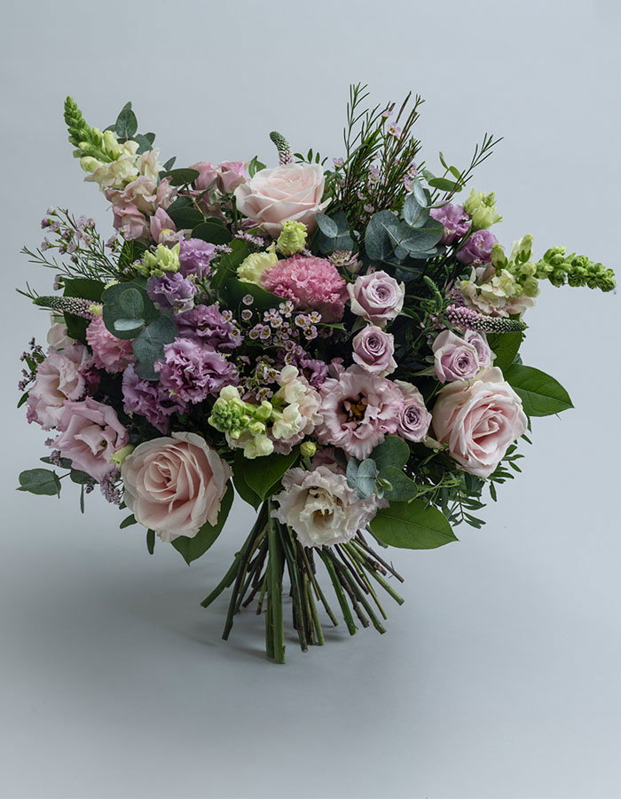 Soft pastel bouquet featuring pink roses, purple carnations, white flowers, and eucalyptus greenery tied with natural stems