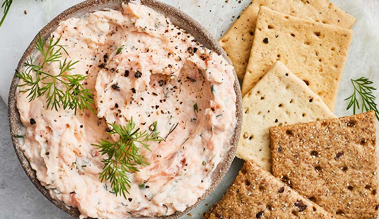 Bowl of creamy p&acirc;t&eacute; garnished with fresh dill, served with assorted crackers on a marble surface
