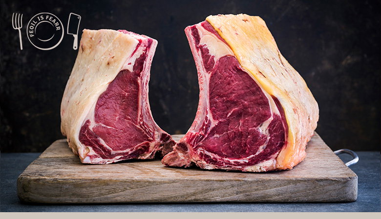 Two large cuts of raw beef ribeye steaks on a wooden cutting board against a dark background, James Whelan Bucther's logo visible in the corner.
