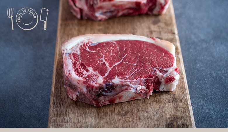 A single thick-cut raw beef ribeye steak on a wooden cutting board, showing marbled red meat with white fat marbling throughout.
