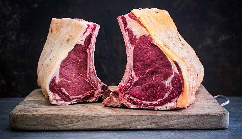 Two large dry-aged bone-in rib cuts of beef on a wooden chopping board