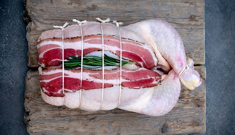 Boned and rolled stuffed chicken with bacon and rosemary, tied with butcher's string on a rustic wooden board