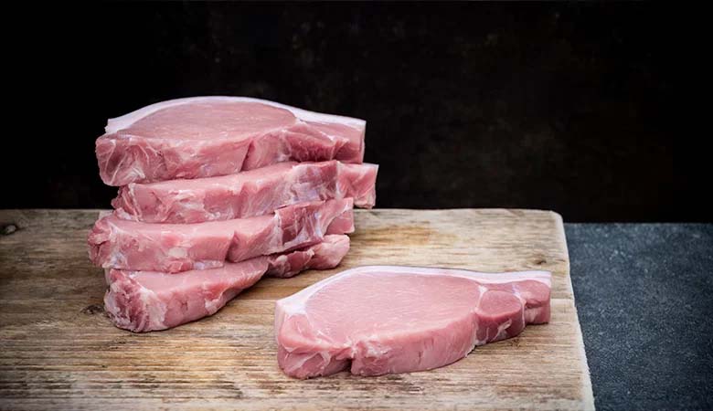 Stack of raw pork loin chops on a wooden board with a single pork chop in the foreground