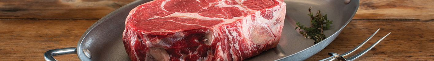 Premium raw ribeye steak on a dark pan with carving fork, showing rich red marbling and white fat streaks, garnished with fresh thyme on a rustic wooden background.