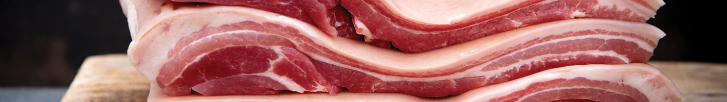 Fresh pork belly strips with alternating layers of pink meat and white fat, arranged on a wooden cutting board displaying the characteristic striped pattern of quality bacon cuts.