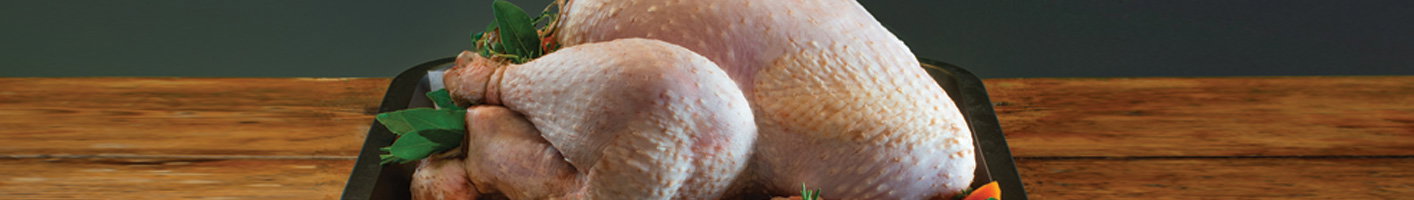 Whole raw chicken positioned on a dark cutting board, garnished with fresh herbs, showing the pale skin and natural shape of farm-fresh poultry ready for preparation.