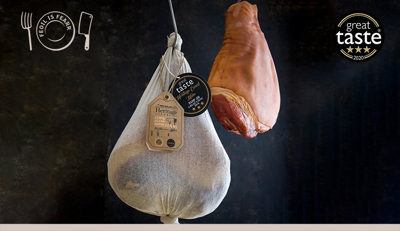 Two cured hams hanging against a dark background - one wrapped in white cloth with heritage tags, one unwrapped showing the natural cured exterior, with a "Great Taste" award badge visible.