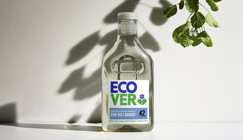 An Ecover glass bottle of concentrated non-bio laundry detergent placed on a white surface with natural plant shadows cast across the scene.