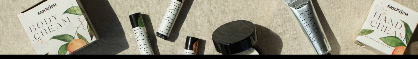 An artfully arranged flat lay of Nourish skincare products including tubes, jars, and boxes with green leaf branding, scattered on a neutral linen background with natural plant elements.