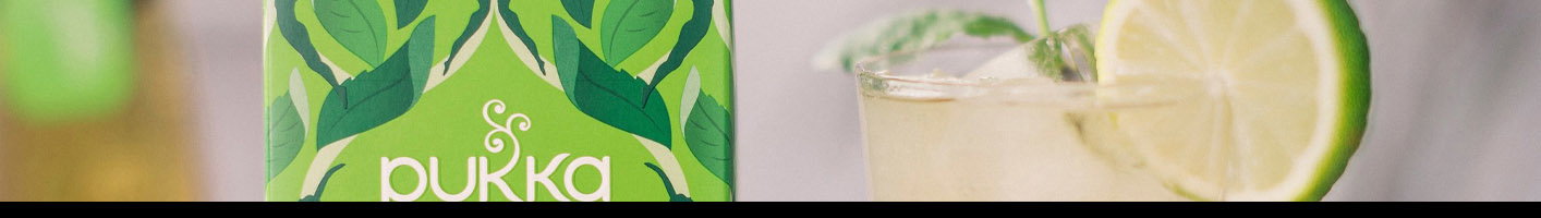 A glass of iced herbal tea with lime garnish and mint leaves next to a Pukka Three Mint Organic tea box featuring green leaf patterns on the packaging.
